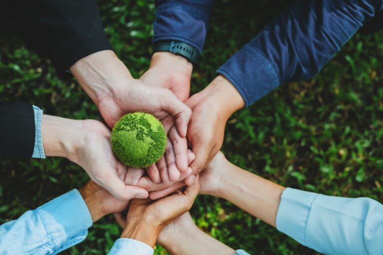 Handen van meerdere mensen die samen een groene wereldbol vasthouden als symbool voor duurzaamheid en gezamenlijke verantwoordelijkheid in de retailsector.